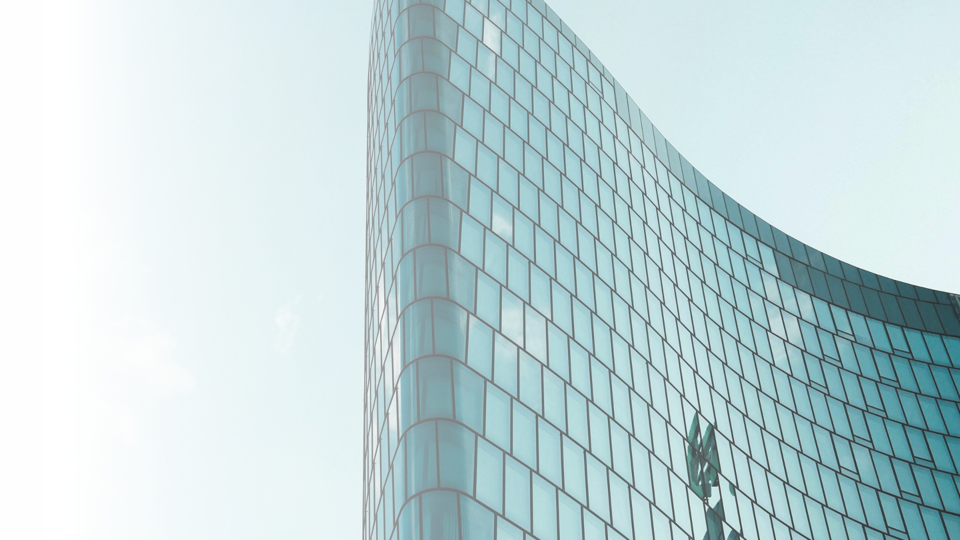 Curved glass office building with blue-tinted windows against a pale sky.
